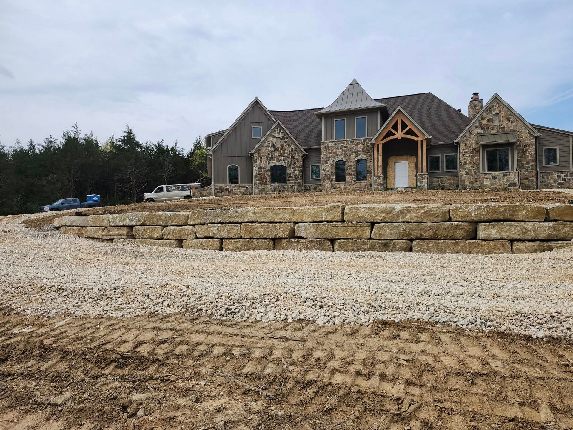 Stone-clad house on a raised bed of gravel. A retaining wall of large stone blocks lines the slope.