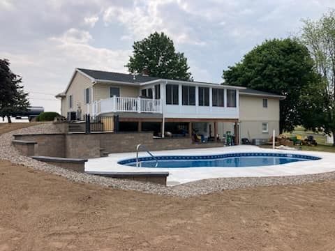 Backyard with a swimming pool, retaining walls, and a two-story house with a deck and sunroom.