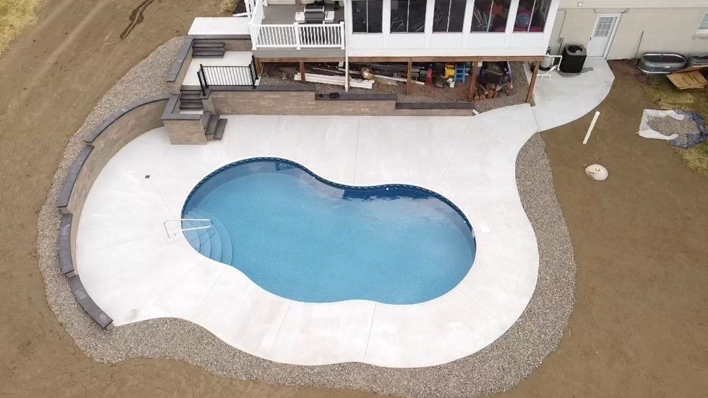 Aerial view of a backyard with a kidney-shaped swimming pool surrounded by a concrete patio and a rock retaining wall.