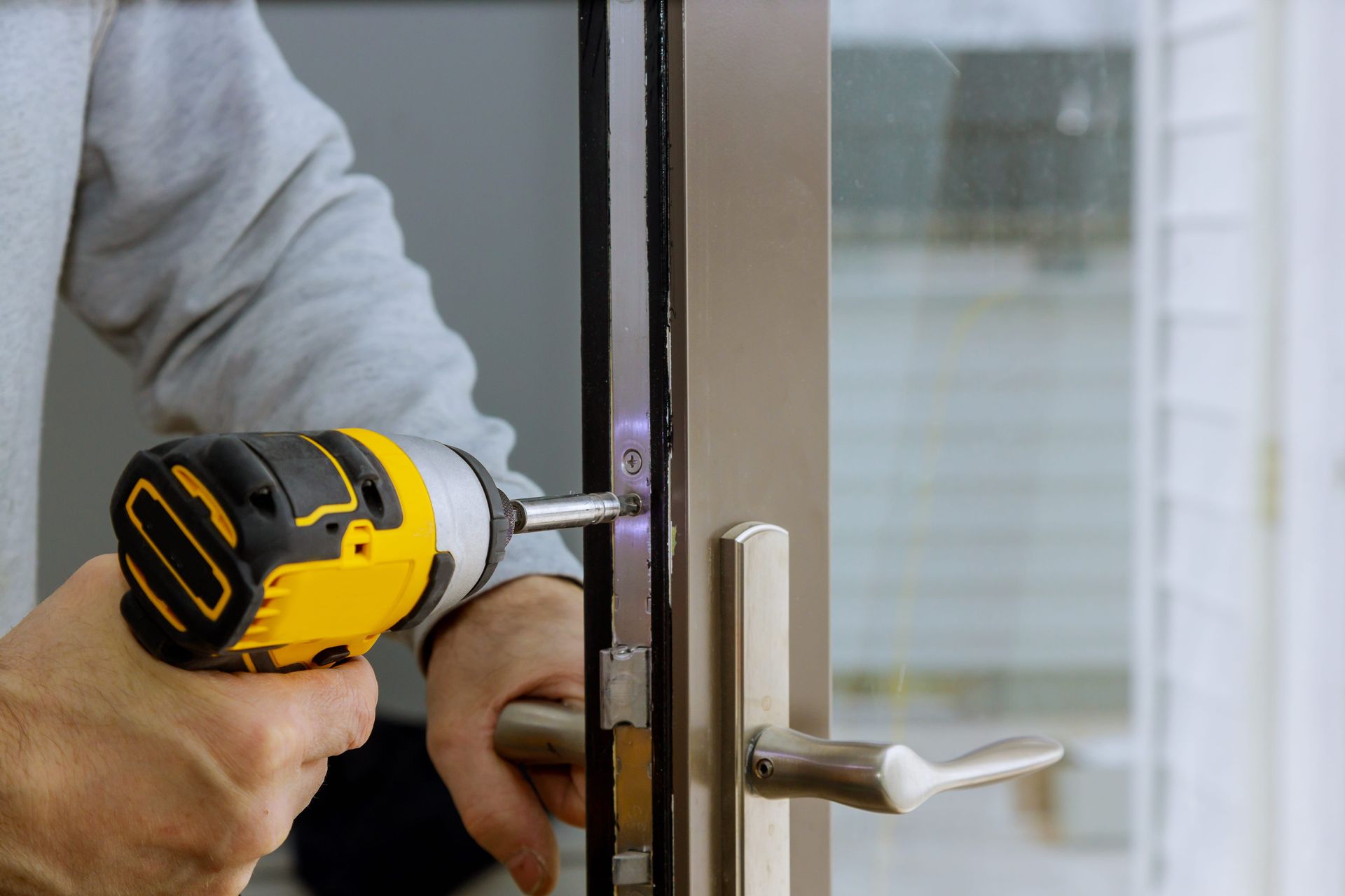 Person using a yellow cordless drill to install a door lock on a glass door