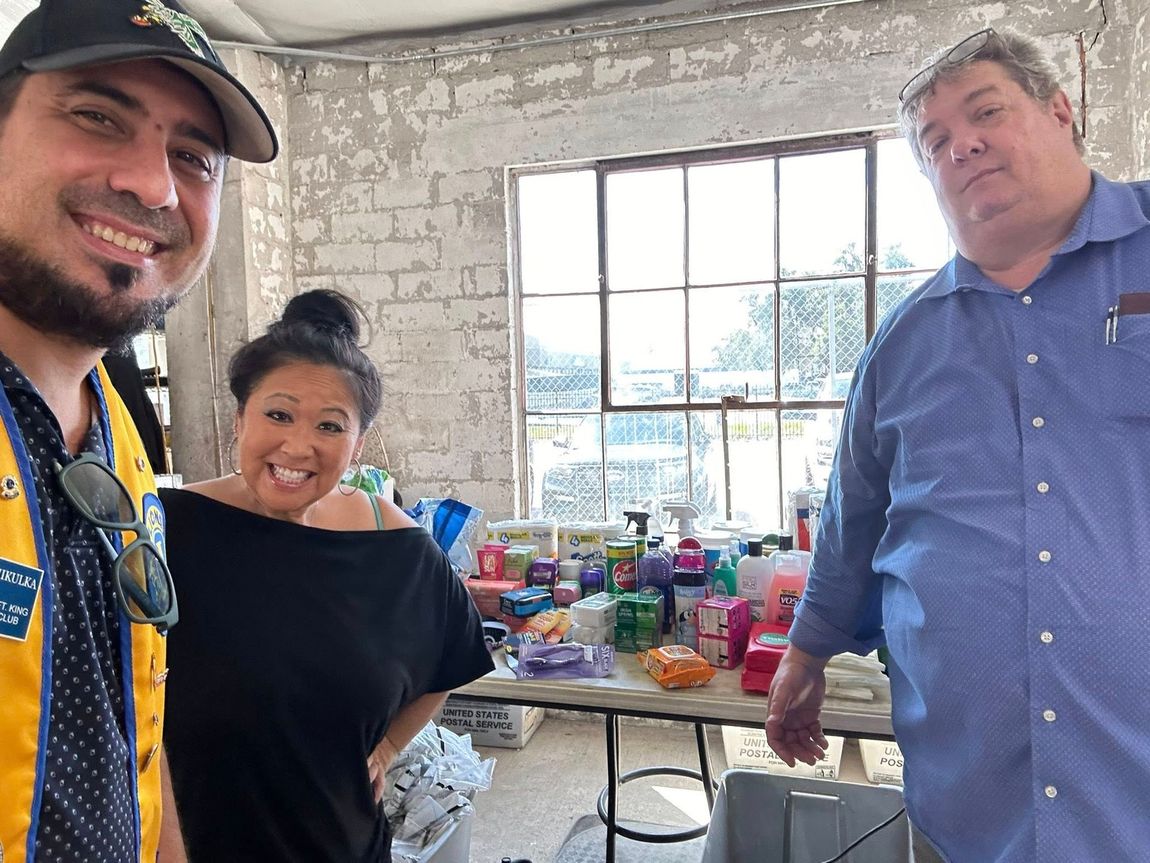 Three people smile near a table with supplies in a brightly lit room.