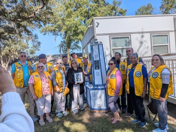Group of people in yellow vests pose with a tall, blue monument outdoors.