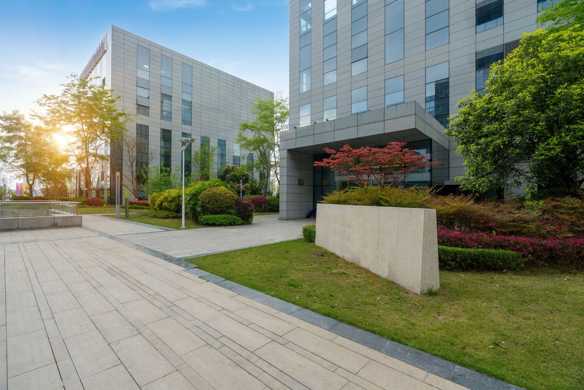 Modern office buildings with a landscaped courtyard, paved walkway, and green lawns at sunset