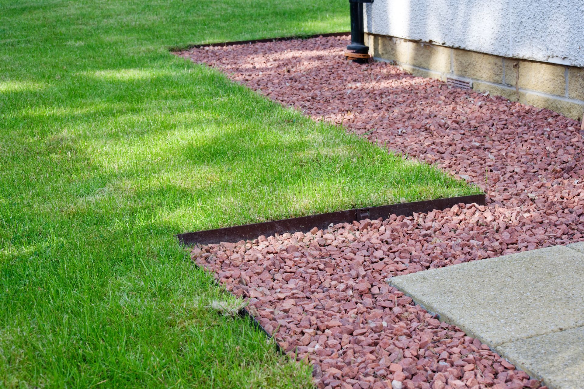 Mulch-lined walkway beside green lawn and a building wall