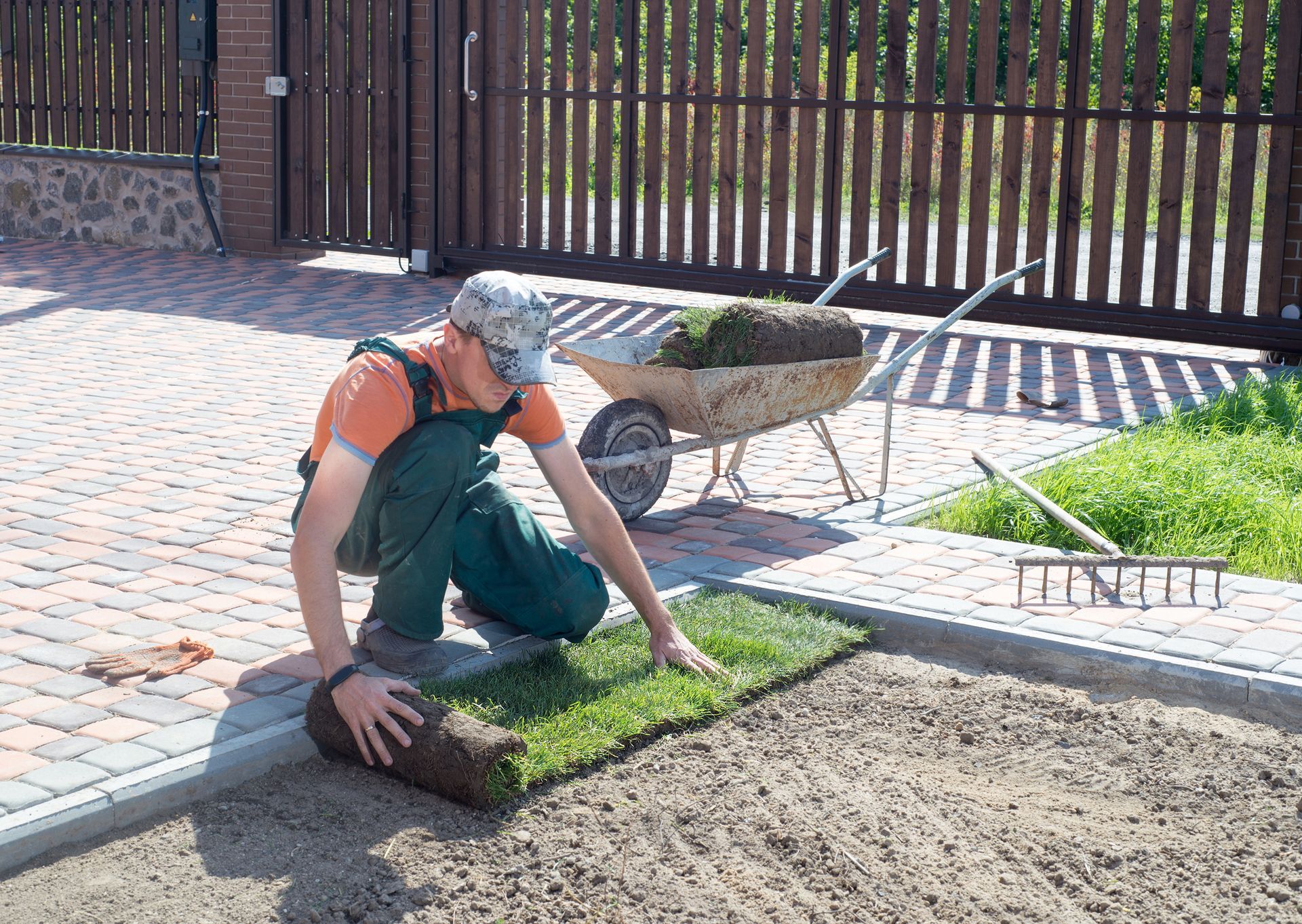 Person laying turf in a yard with a wheelbarrow and garden tools nearby