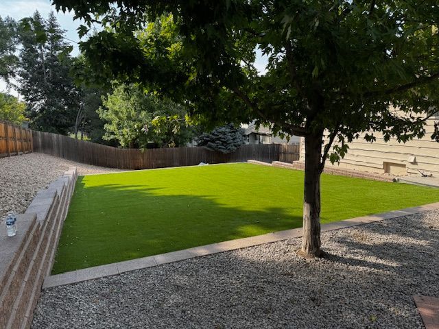 Landscaped backyard with bright green lawn, gravel paths, trees, and a wooden fence.