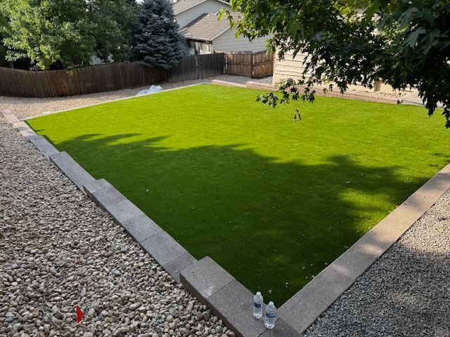 Backyard with bright green lawn, gravel border, and a house in the background.