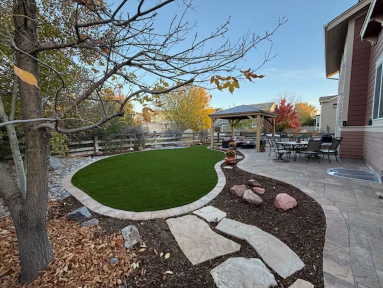 Backyard patio with curved stone path, green lawn, trees, and an outdoor seating area near a house