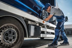 Mechanic working under a blue truck in a garage, inspecting the side panel.