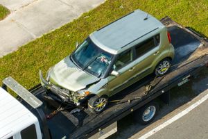 Green SUV strapped on a flatbed tow truck on a road shoulder