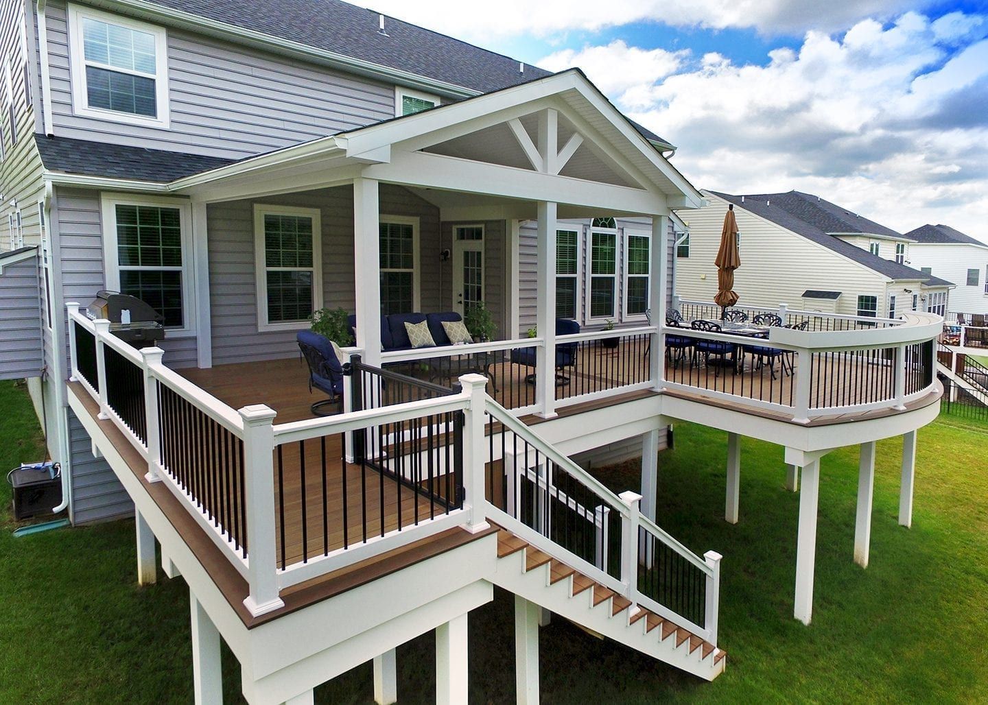 A multi-level wood deck with a covered patio area, white railings, and stairs leading down to a green lawn.