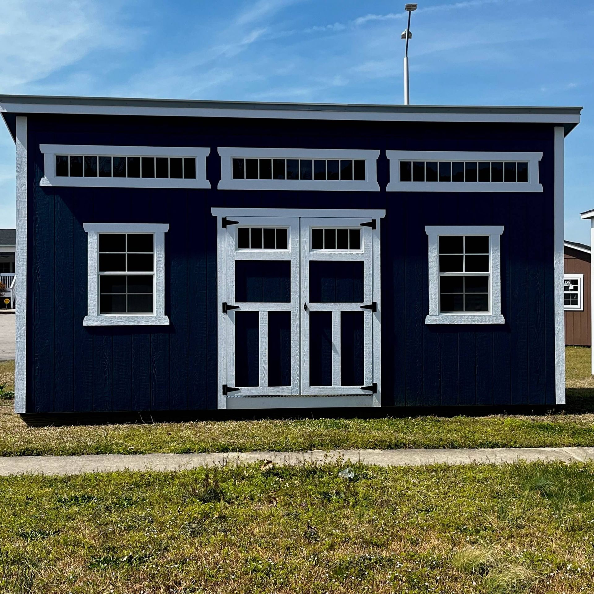 A dark blue shed with a flat roof, white trim, double doors, and several small rectangular transom windows.