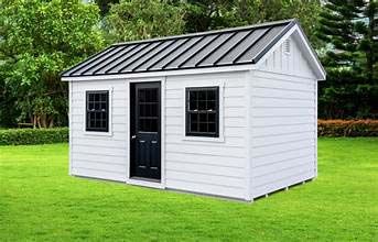 A white, rectangular shed with a black roof, black door, and two black-framed windows, situated on a green lawn.
