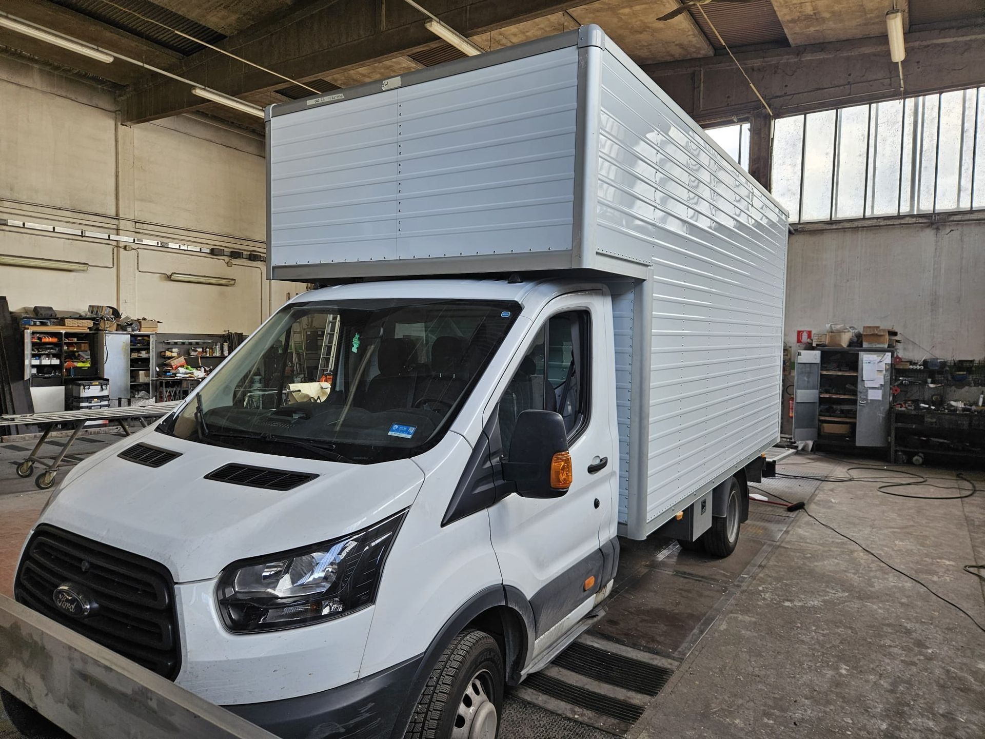 Un furgone bianco parcheggiato all'interno di un'officina, sotto luci industriali.