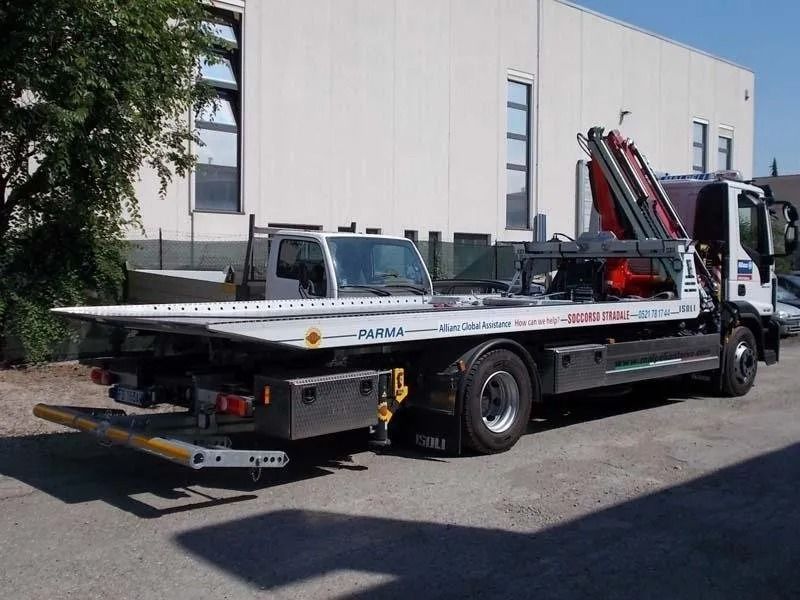 Carro attrezzi con pianale parcheggiato davanti a un edificio bianco in una giornata di sole.