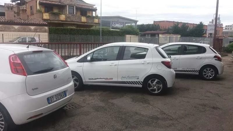 Tre auto hatchback bianche parcheggiate in un piazzale accanto a una recinzione e ad alcune case.