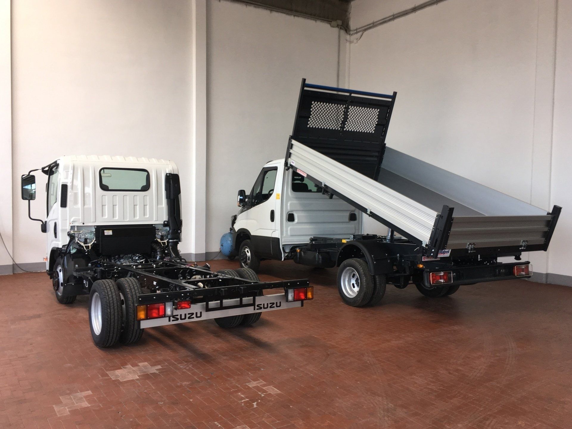 Due piccoli autocarri ribaltabili con cassone rialzato parcheggiati all'interno di un garage simile a un magazzino.