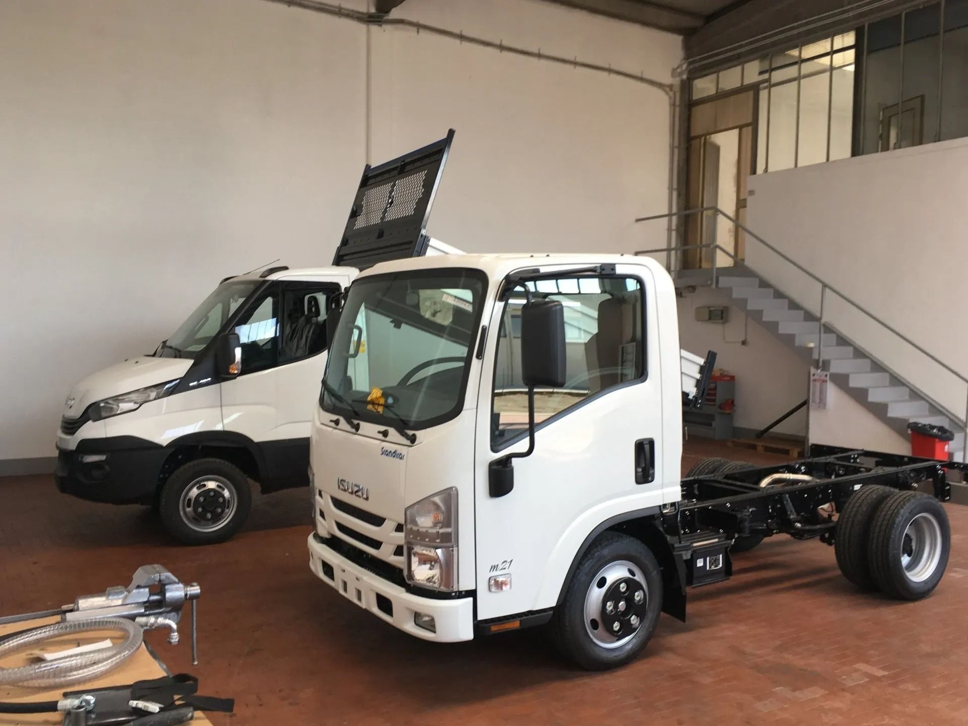 Due camion commerciali bianchi parcheggiati in un garage, uno con telaio cabinato in primo piano e uno furgone sullo sfondo.