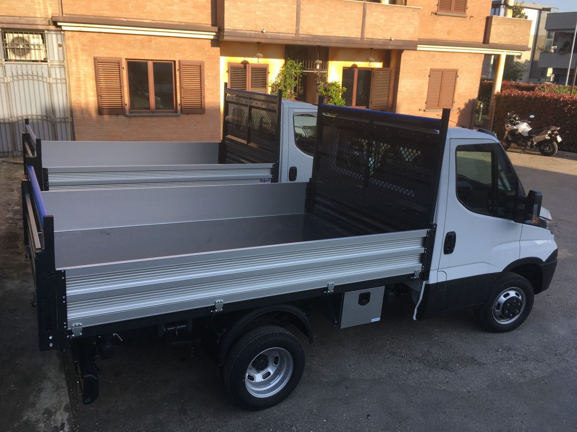 Camion bianco a pianale ribassato parcheggiato accanto a un edificio in mattoni in pieno giorno