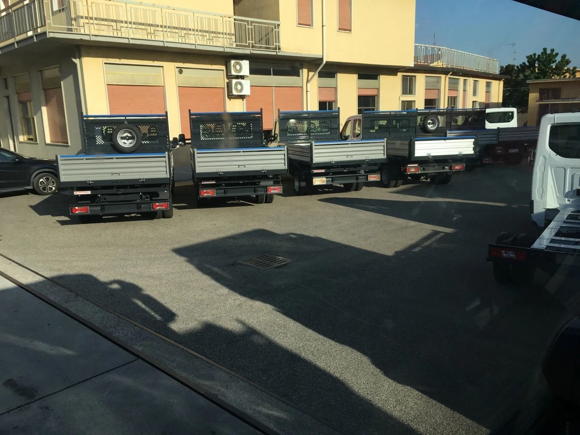 Diversi camion a pianale ribassato neri parcheggiati fuori da un edificio giallo in un parcheggio soleggiato