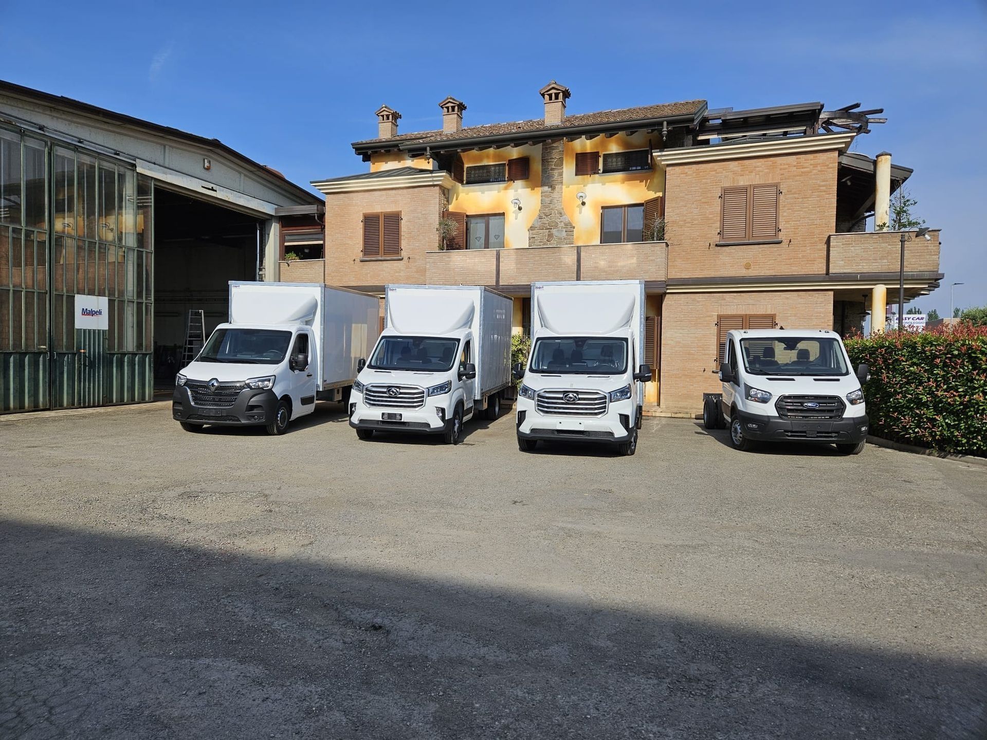 In una giornata di sole, quattro furgoni bianchi erano parcheggiati davanti a un edificio rustico a due piani.