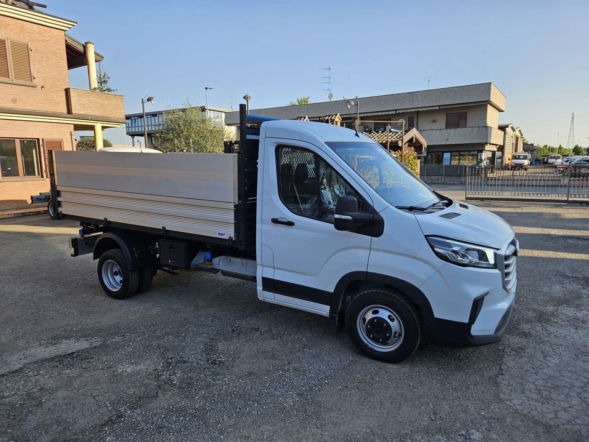 Camion bianco a pianale ribassato parcheggiato su ghiaia in una zona industriale.