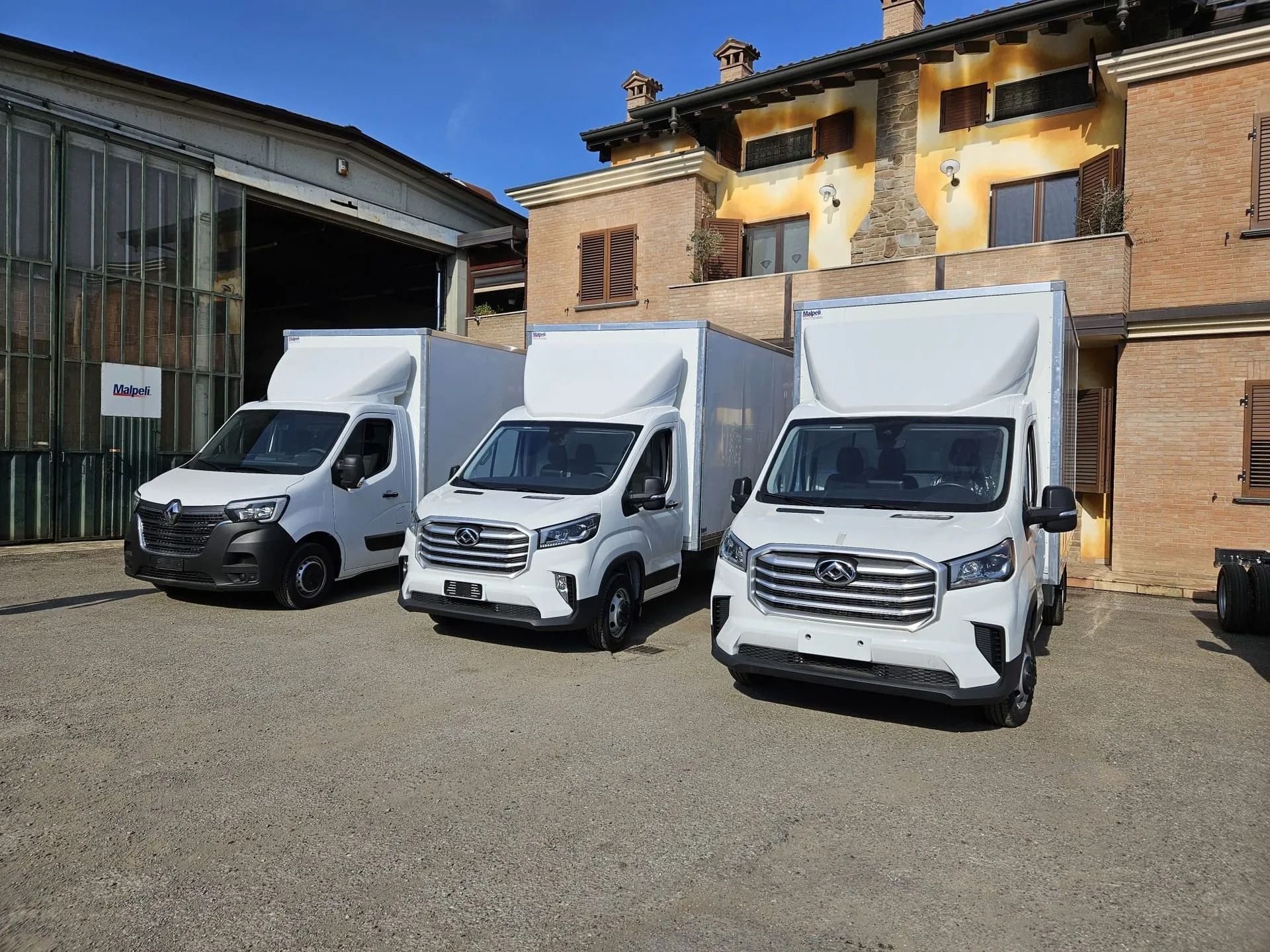 In una giornata di sole, tre furgoni bianchi per le consegne erano parcheggiati davanti a un edificio in mattoni.