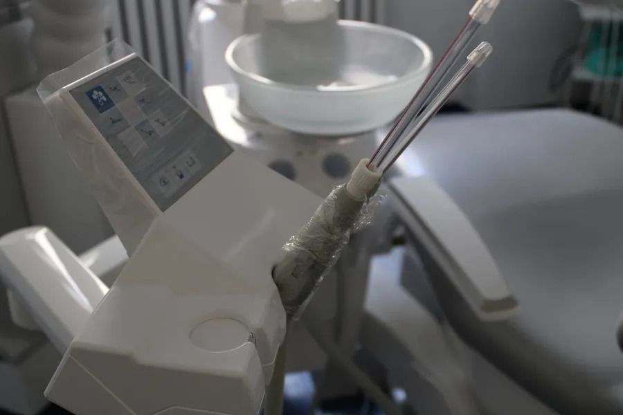 Strumenti odontoiatrici su un vassoio bianco nello studio dentistico, con una piccola ciotola e una poltrona per il paziente visibili.