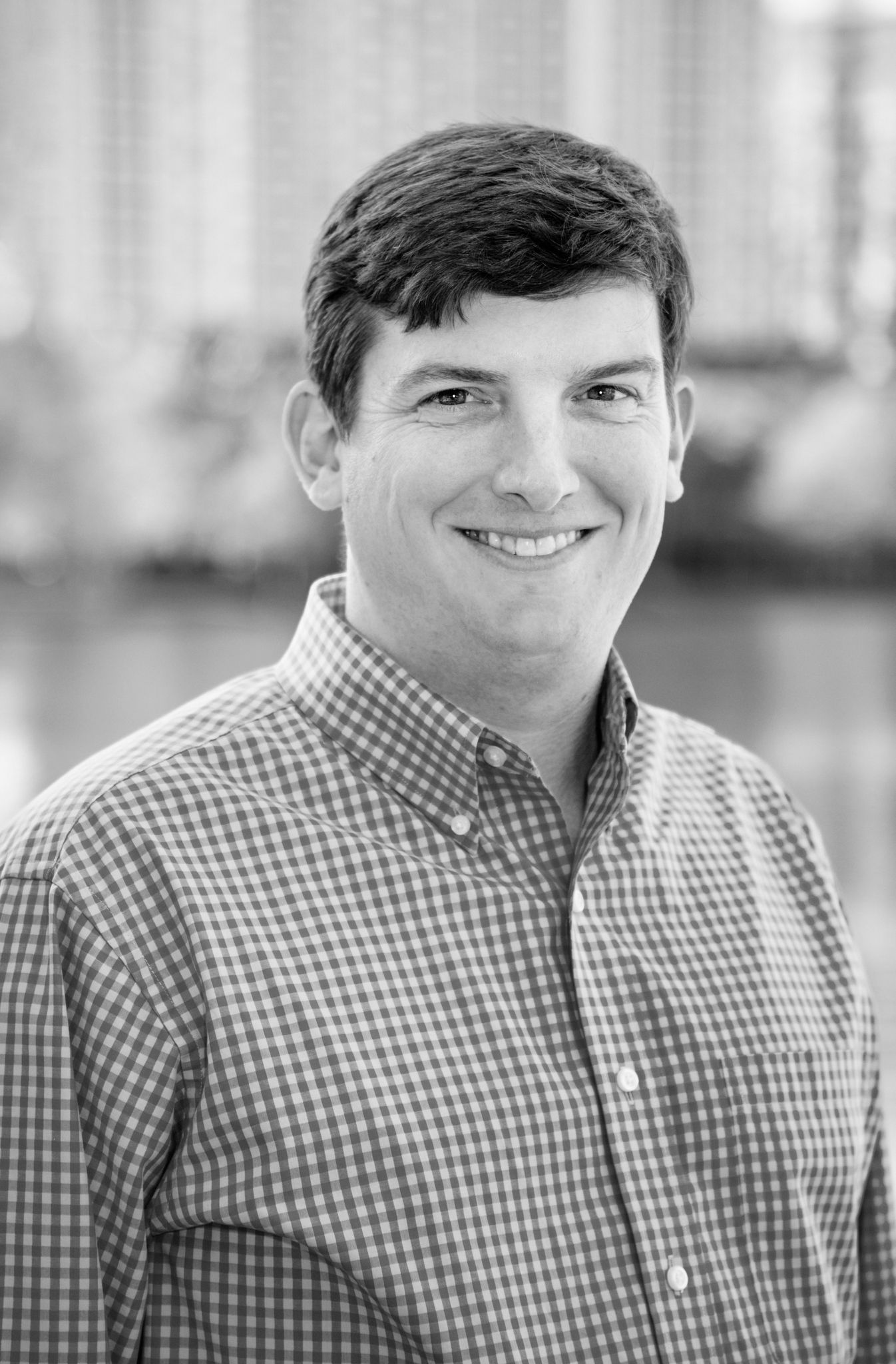 A man in a white shirt is smiling in a black and white photo.