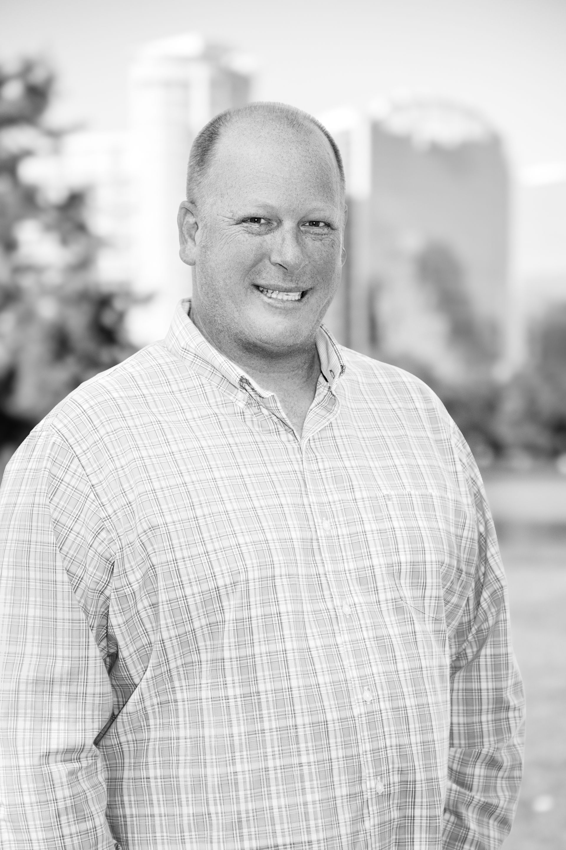 A man in a plaid shirt is smiling in a black and white photo.