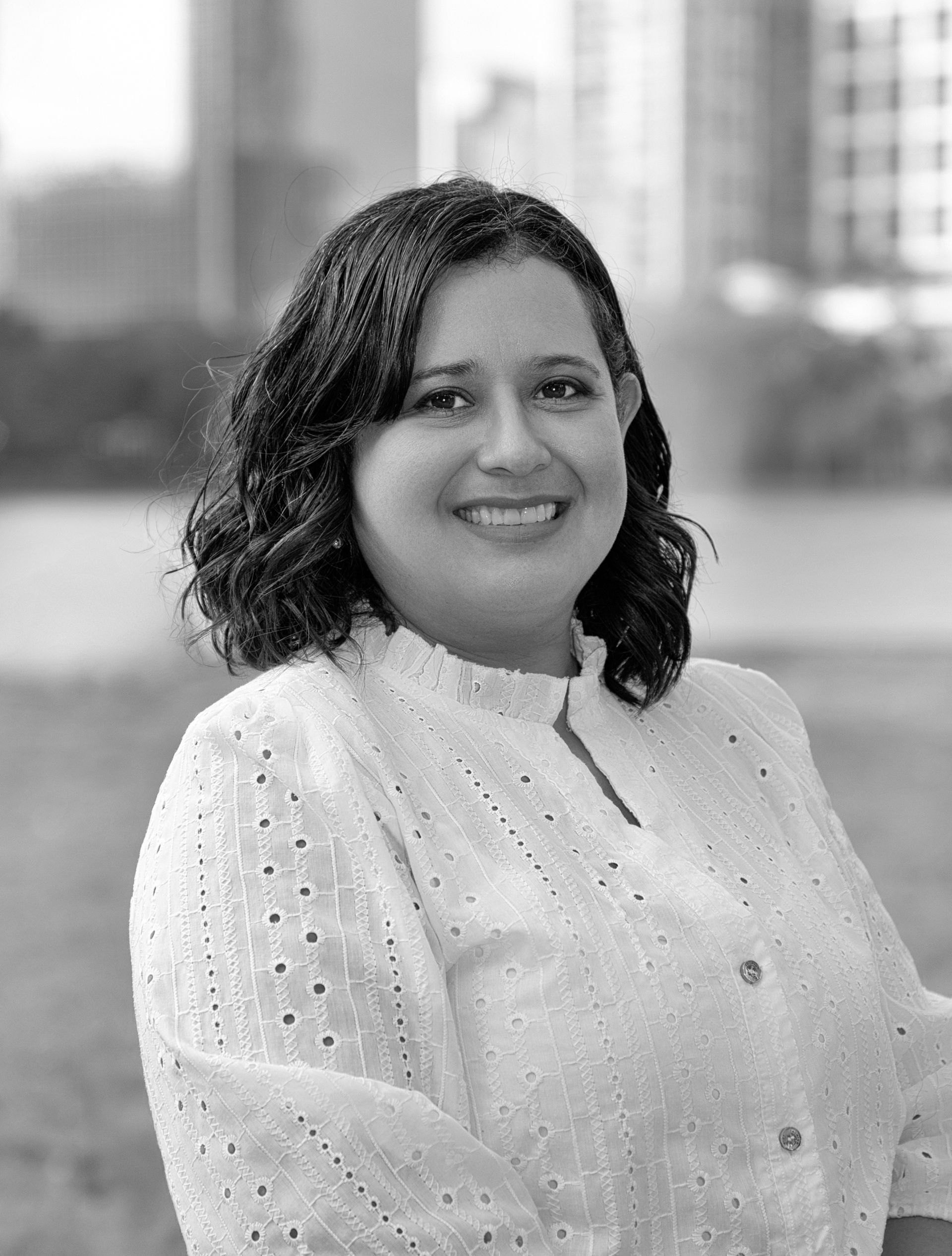 A woman in a white shirt is smiling in a black and white photo.