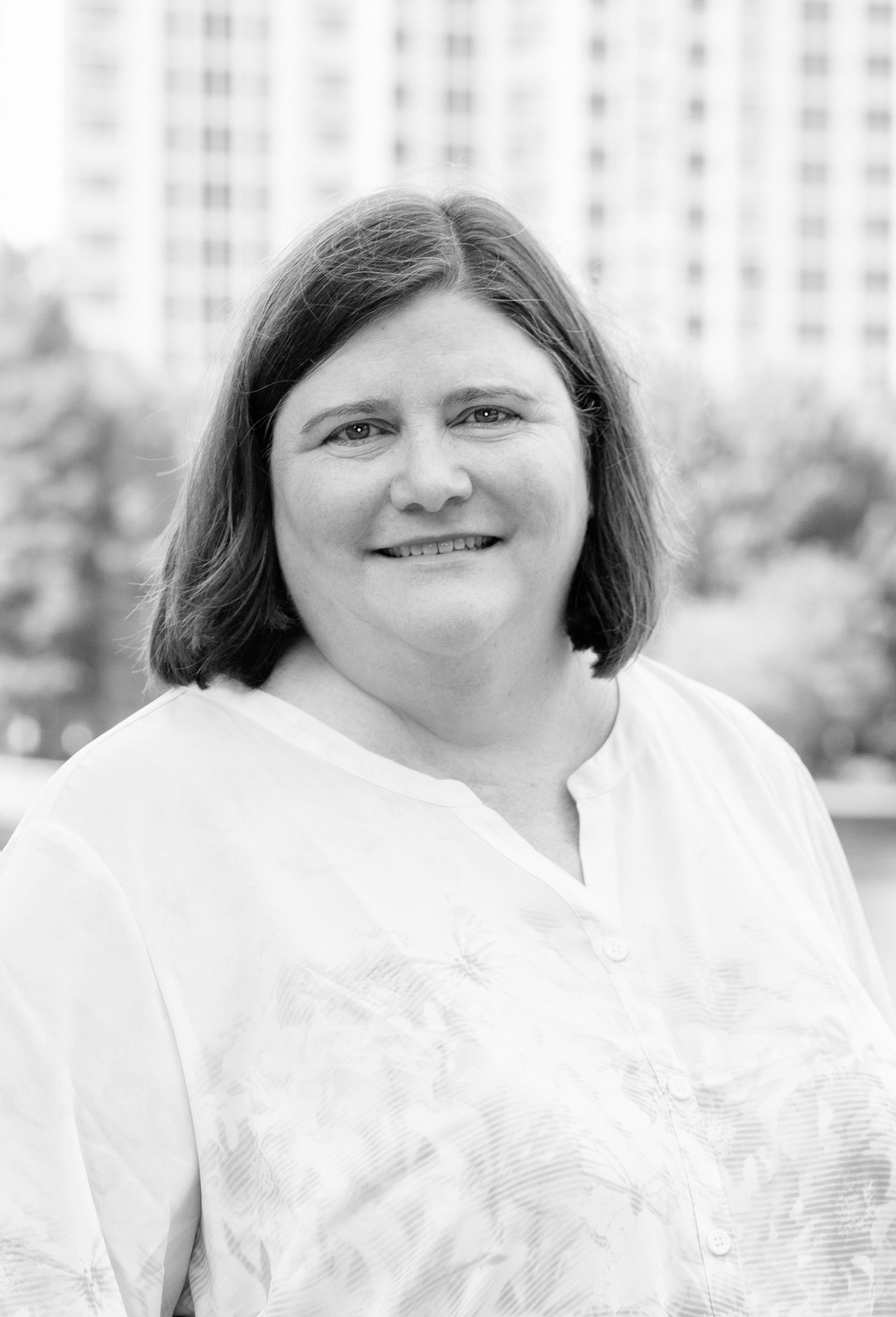 A woman in a white shirt is smiling in a black and white photo.