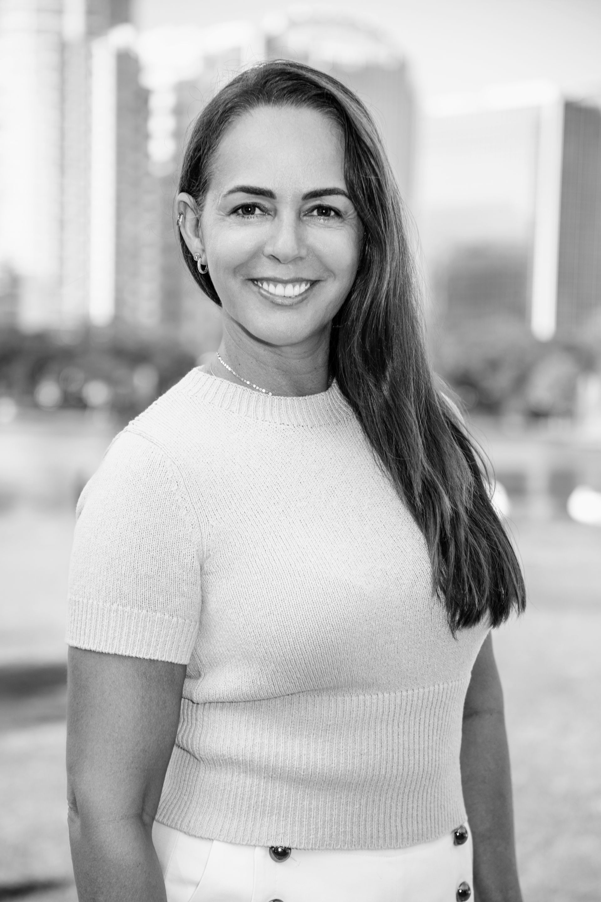 A black and white photo of a woman smiling in front of a city skyline.