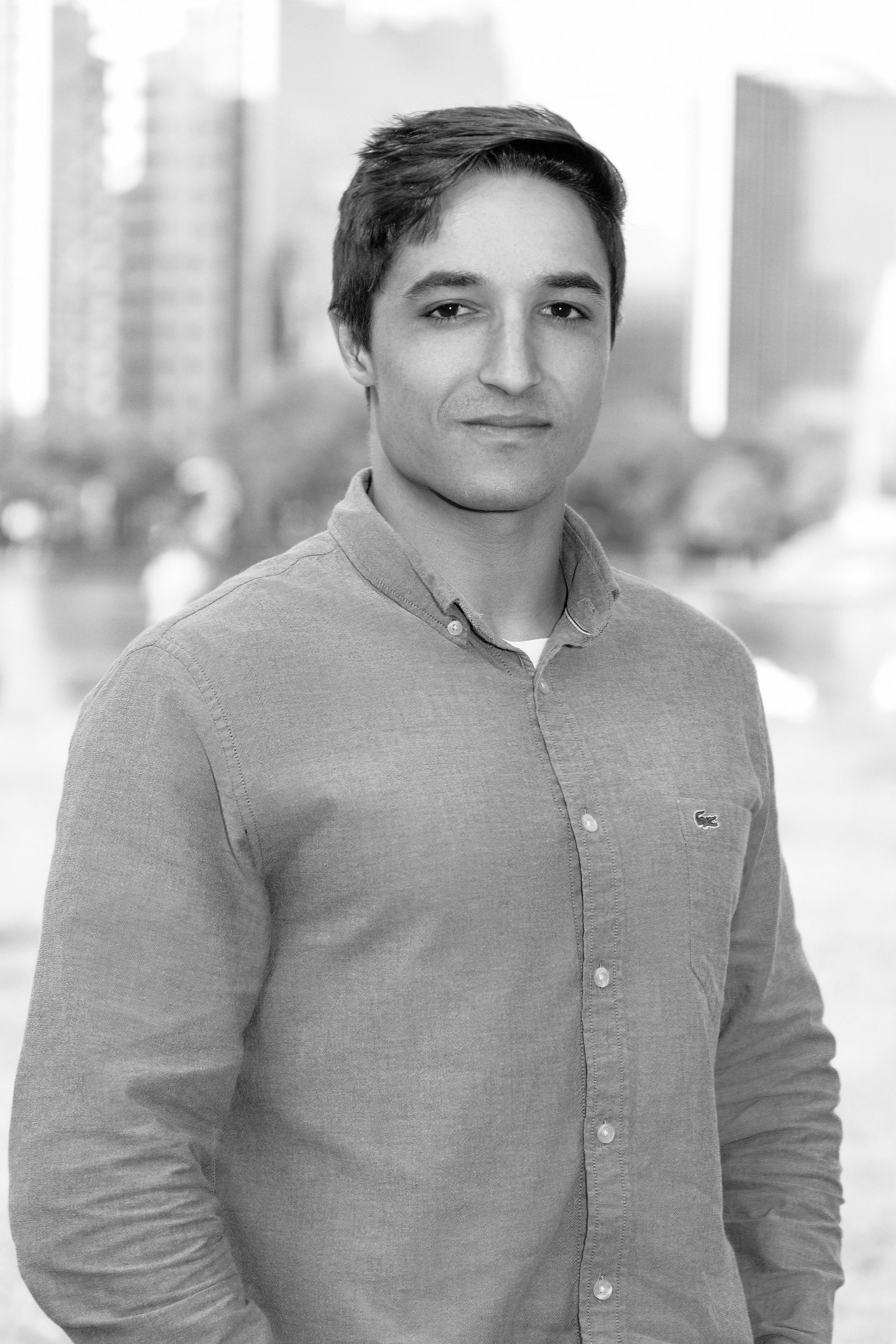 A man in a grey shirt is standing in front of a city skyline in a black and white photo.