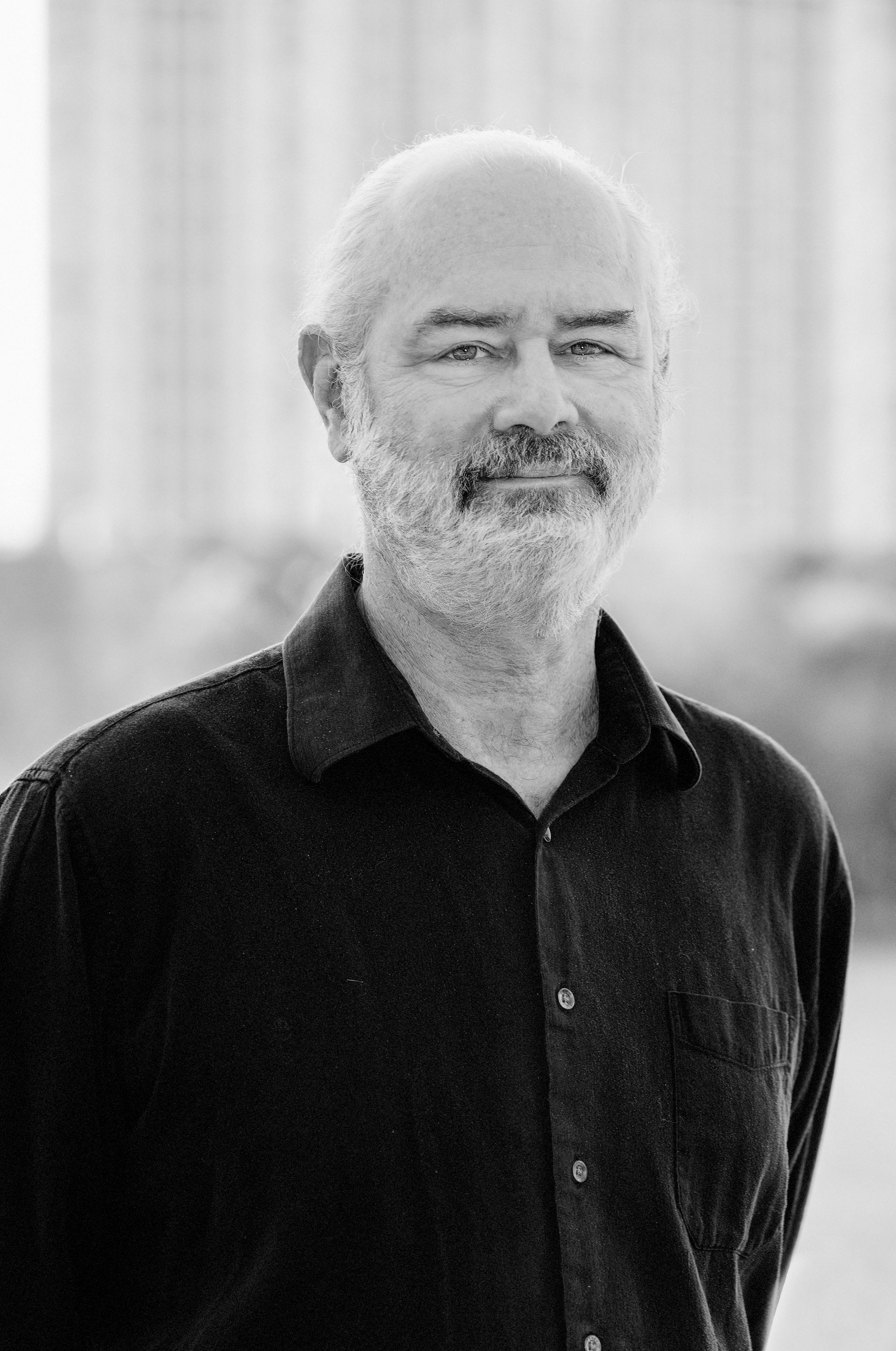 A black and white photo of a man with a beard wearing a black shirt.