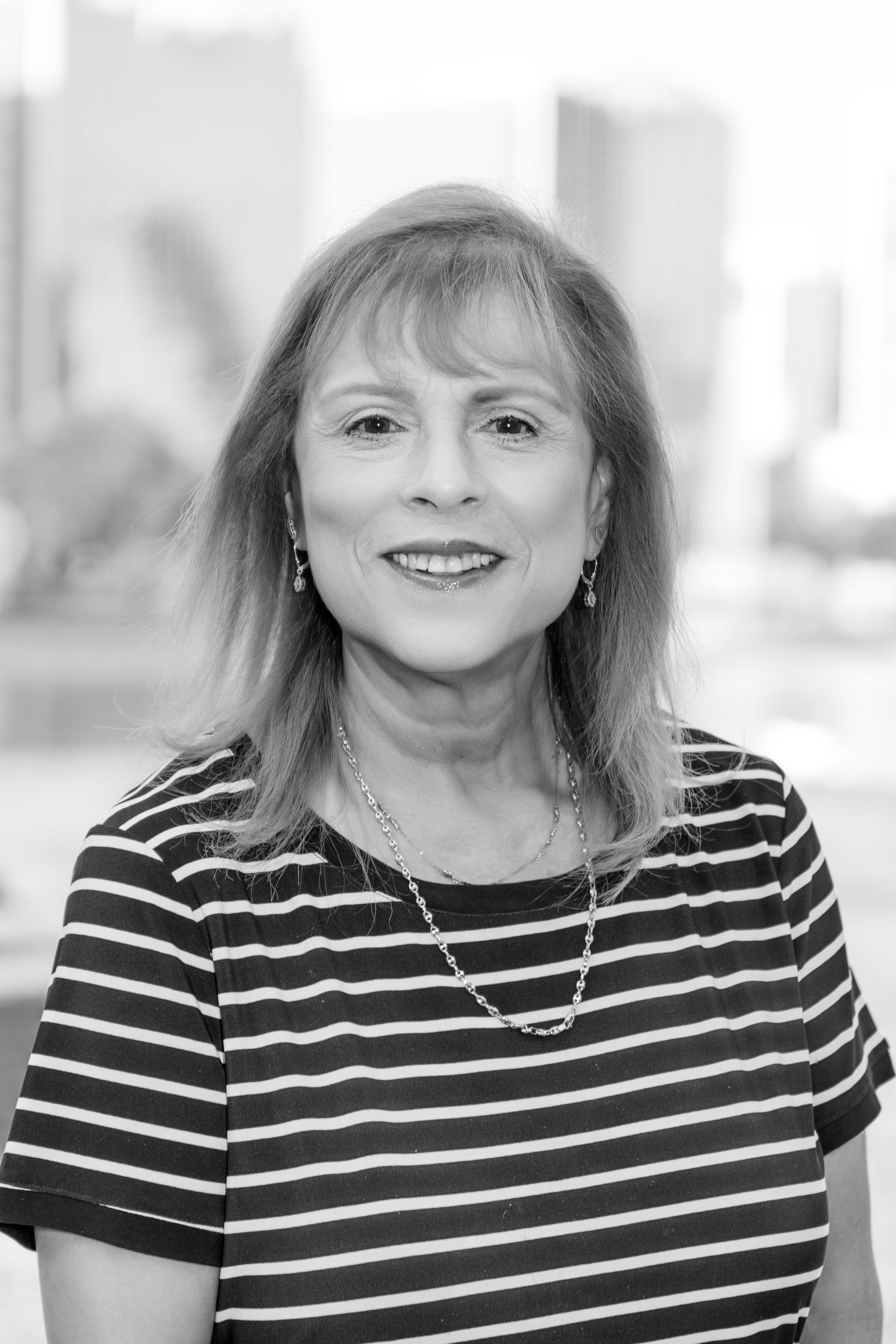 A woman in a striped shirt is smiling in a black and white photo.