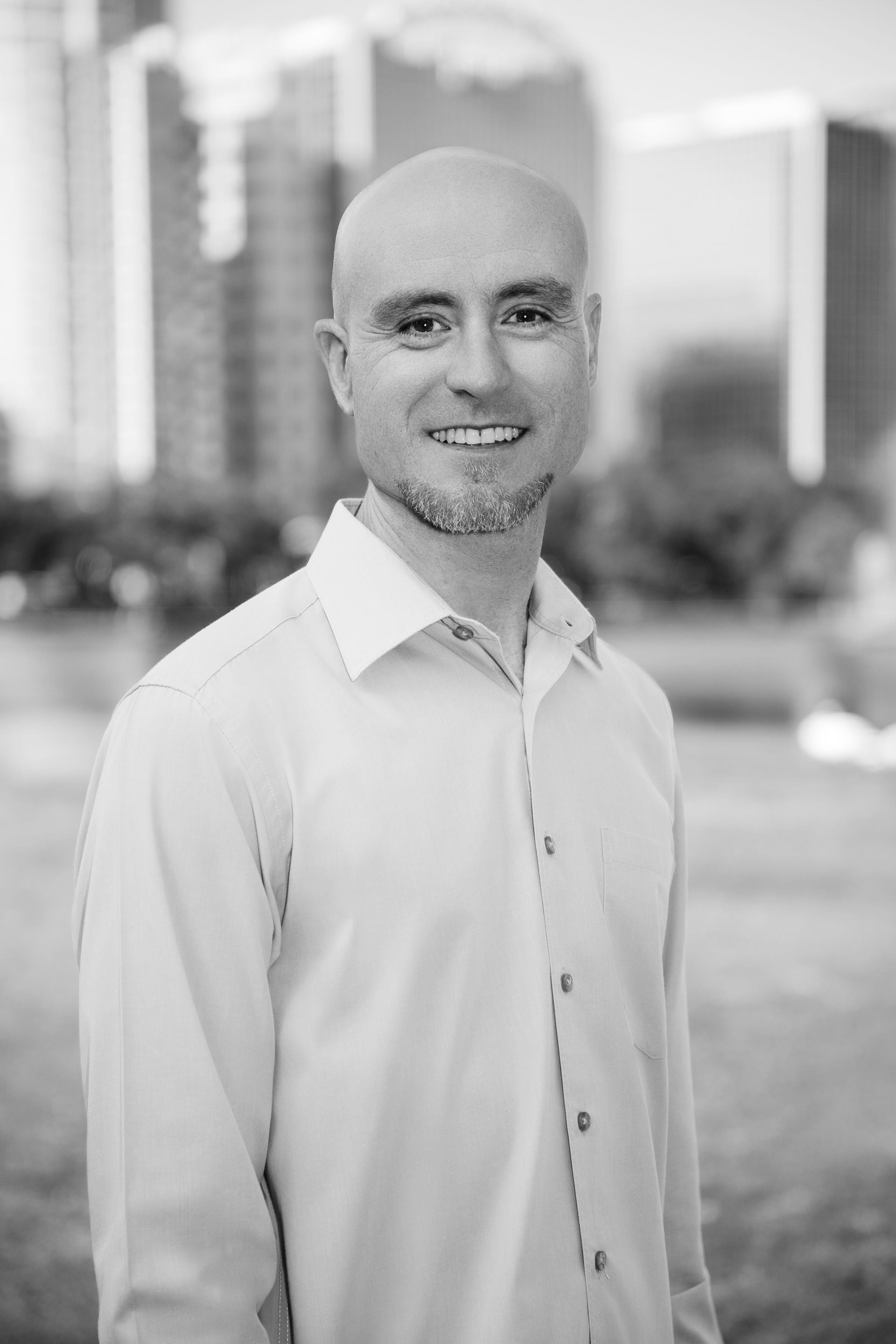 A man in a white shirt is smiling in a black and white photo.