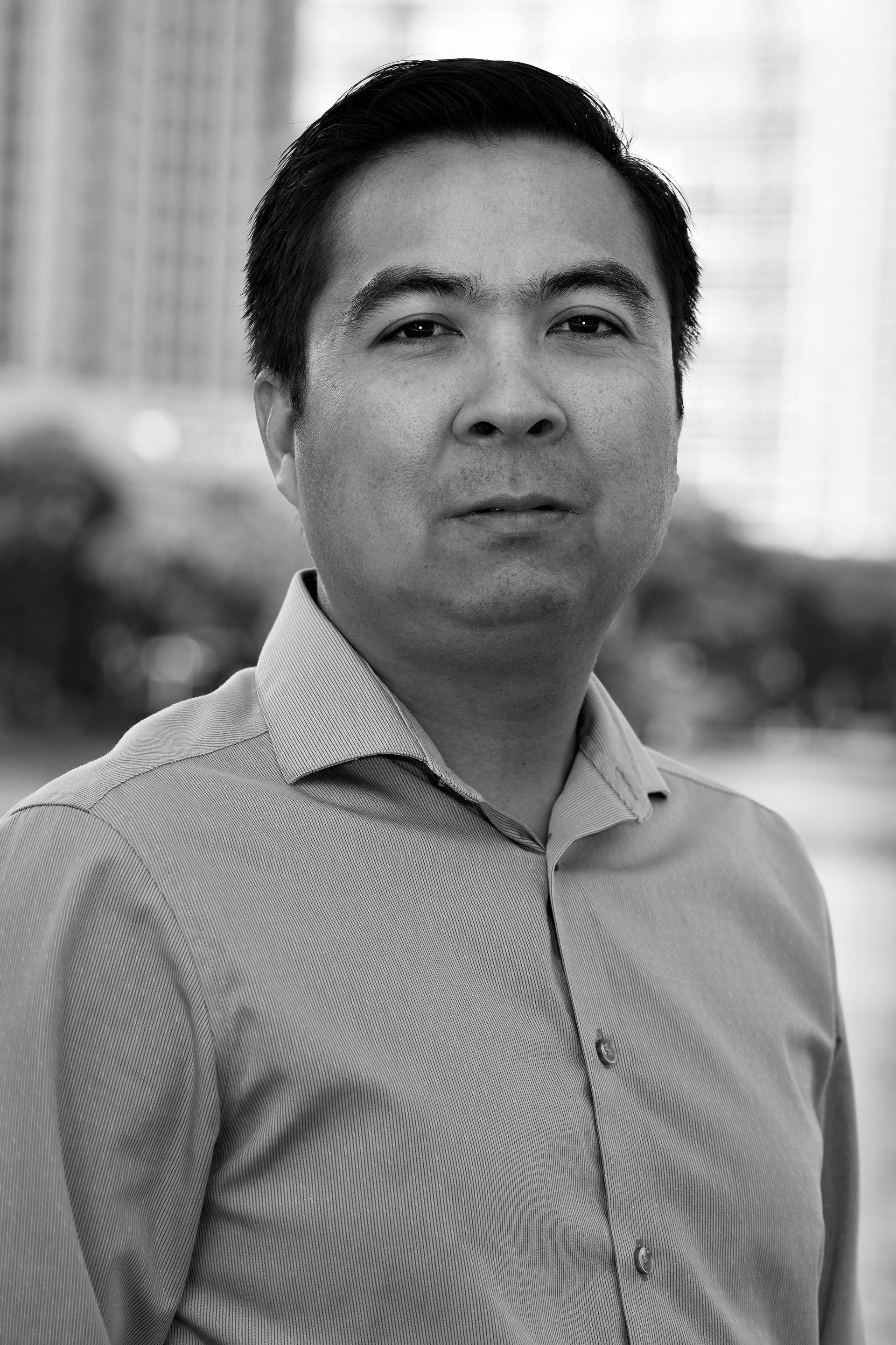 A man in a striped shirt is standing in front of a building in a black and white photo.