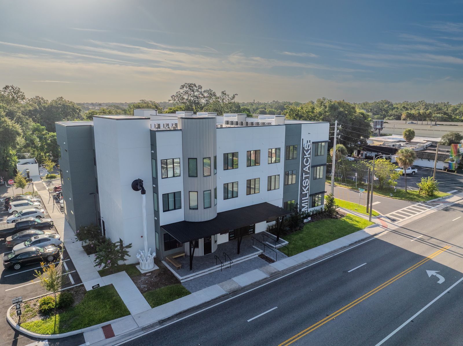 Modern three-story building with a gray and white facade, sidewalk, cars parked nearby.