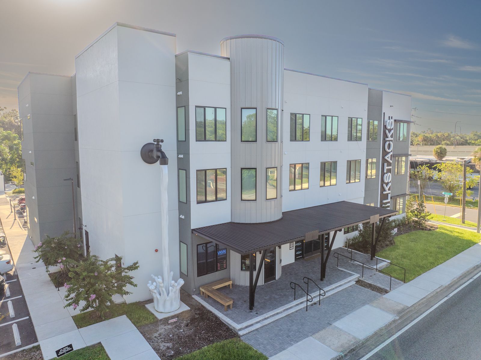 Modern three-story building with gray and white facade, ELKSTACK signage, entrance with canopy, and surrounding greenery.