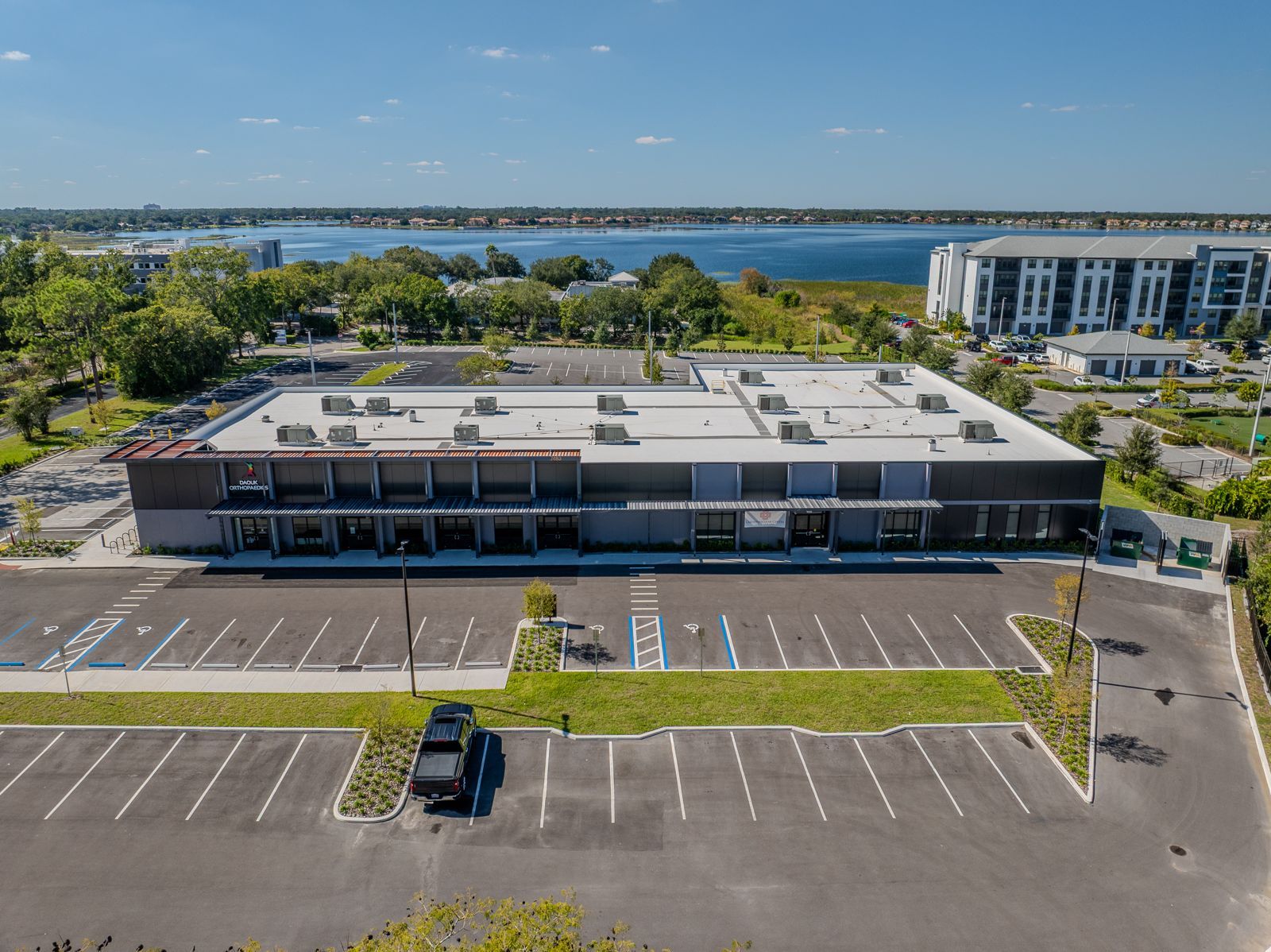 Aerial view of a commercial building with a large parking lot, waterfront in the background.