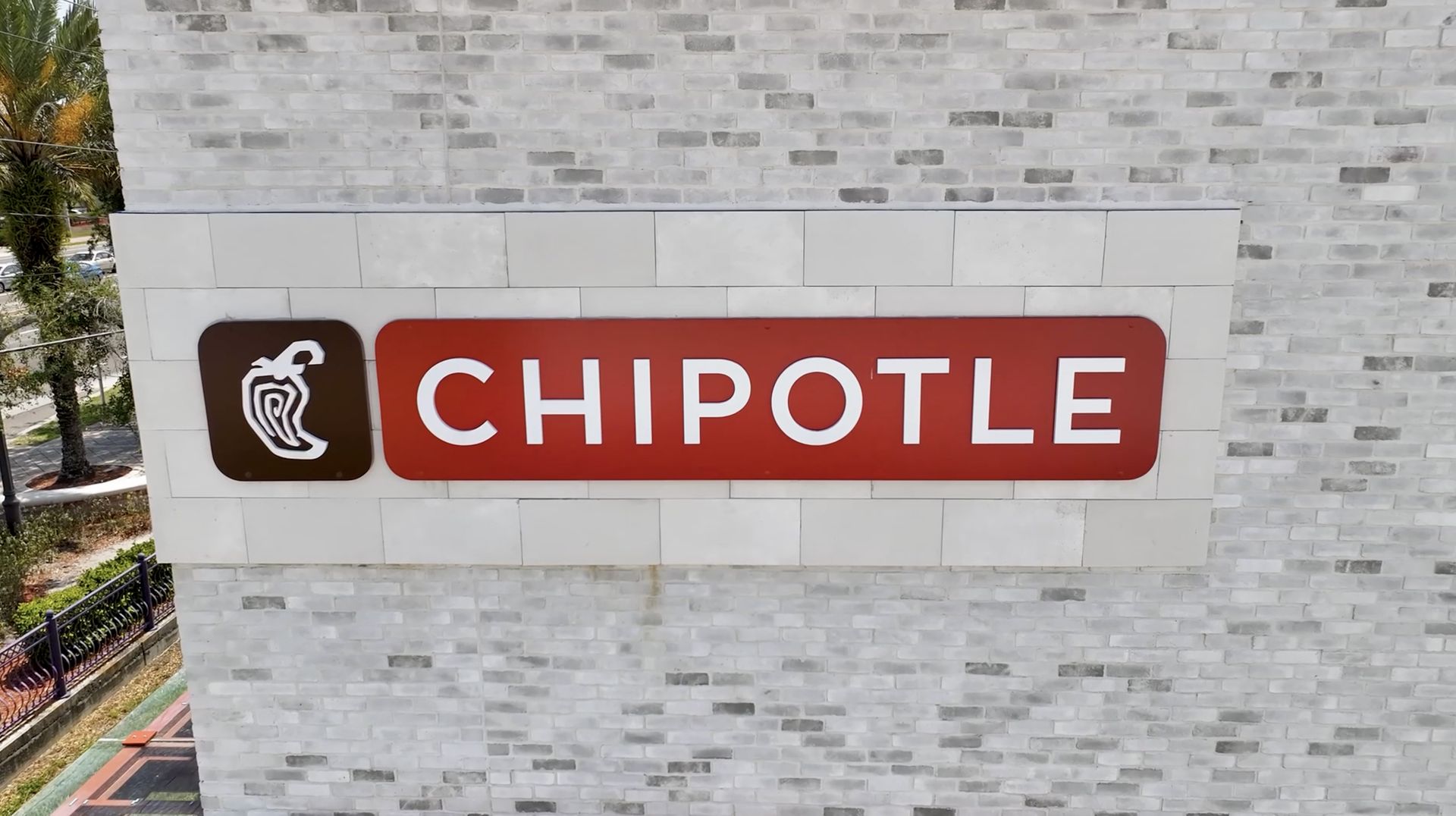 A chipotle sign is on a white brick wall