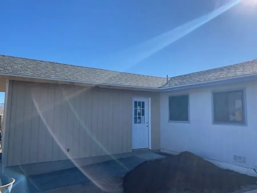 Small white house exterior with a front door, window, blue sky, and a pile of dirt in the foreground