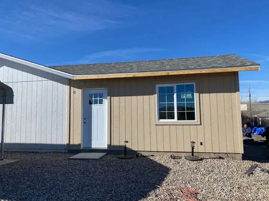 Small beige building with white door and window on gravel under a blue sky