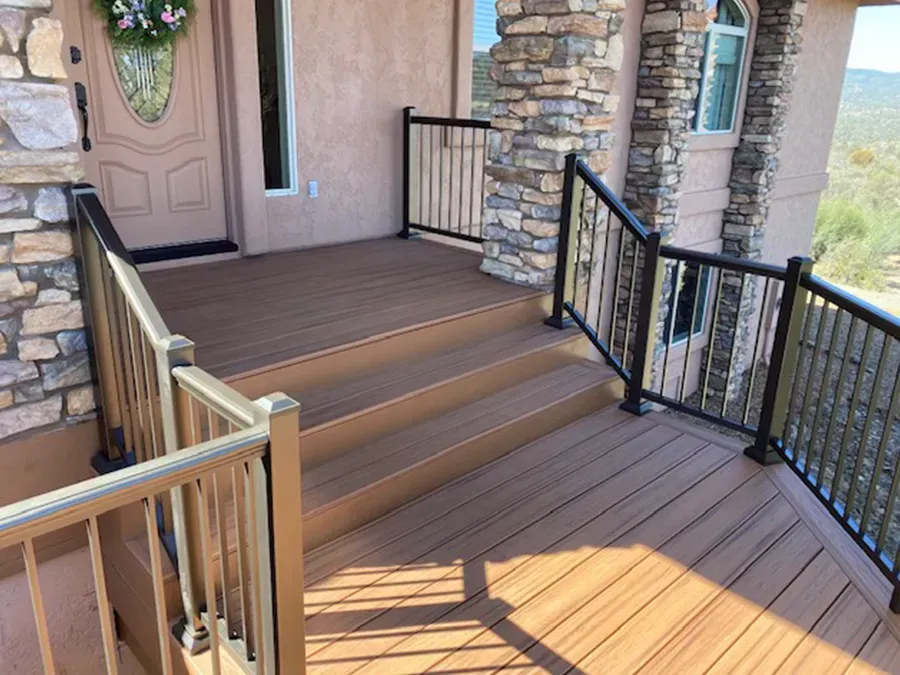 Front porch with brown decking, stone columns, black railings, and a tan front door with a wreath.