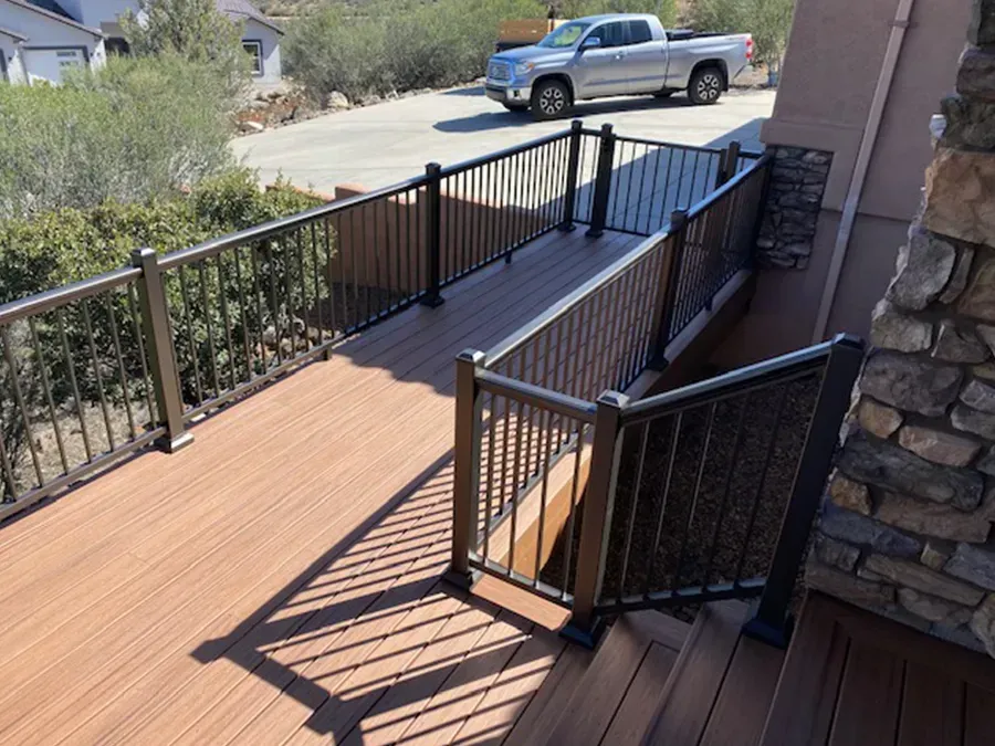 Accessible wooden ramp with black railings leading to a house entrance beside a stone wall.