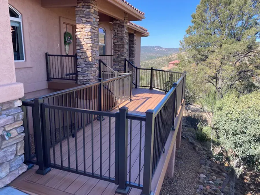 Stone house deck with black metal railings overlooking a wooded hillside and mountains