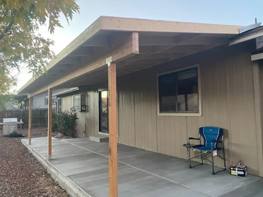 Covered porch beside beige house with concrete patio, wooden posts, and a blue folding chair