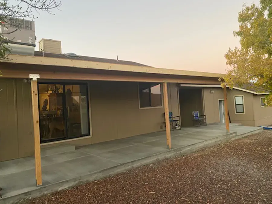 Covered patio attached to a beige house with sliding glass door and gravel yard at sunset