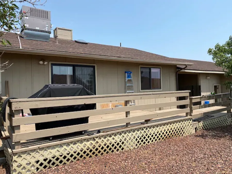 Single-story beige house with a wooden ramp, lattice skirting, and a covered carport under a blue sky